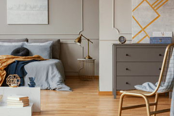 Trendy bedroom interior with grey commode and golden chair