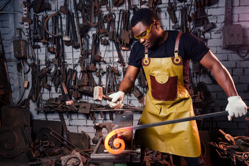 hammer industry small business concept.african american man dressed in historical clothing is hammering on the anvil. A blacksmith forges a metal product - Powered by Adobe