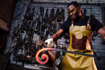 Fototapeta na wymiar handsome african american blacksmith male worker working in workshop,wearing leather apron
