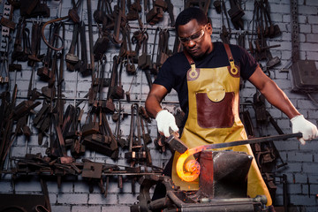 handsome african american blacksmith male worker working in workshop,wearing leather apron