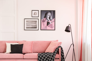 Gallery of posters on empty white wall of bright living room interior with pastel pink settee