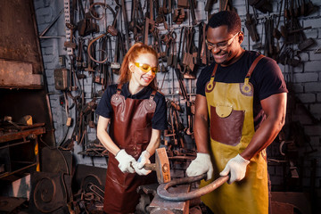 couple in love redhaired ginger young european woman and afro-american man wearing leather apron working blacksmith workshop.small family international business concept