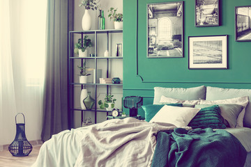 Stylish bedroom interior with double bed and emerald green wall