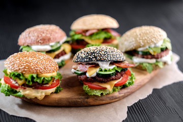 5 handmade burgers with beef, salad, cheese tomatoes, sesame seeds, bacon on black wooden table