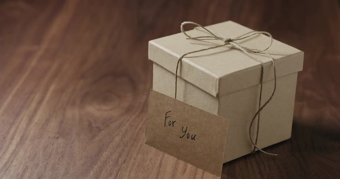 Slow motion man hand put for you card next to brown paper gift box on walnut table