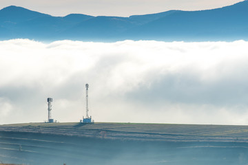Radio antennas in front of dense fog, blue mountains in the background.