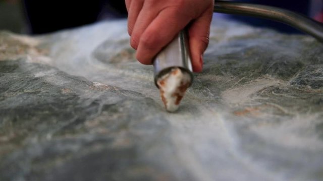 close shot of tourist activity at the Boyne valley tombs. handheld shot of a hand holding a steel mantled carving stone and carving an artisan pattern in limestone. Lower frame copy space.