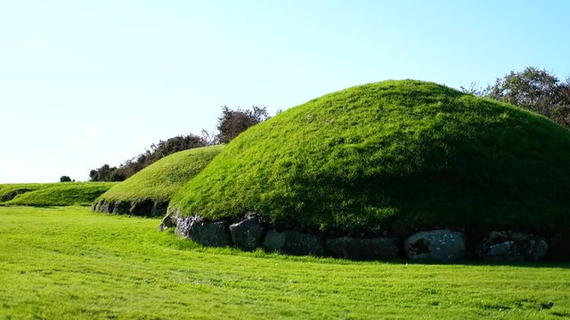 scenic handheld wide shot of a row of green grass covered prehistoric tombs against blue sunny sky in Knowth, one of Irelands famous Boyne Valley Tombs. Copy space and no people.