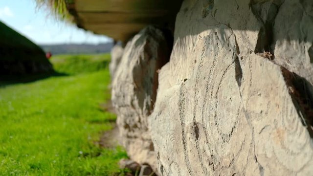 hand held close shot of ancient engravings on Br&uacute; na B&oacute;inne stone wall in Knowth. Sunlight shines on stone carvings in foreground. copy space with green meadows and landscape in the background.