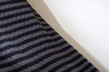 A quilted black and gray striped blanket agains stucco wall at angle.