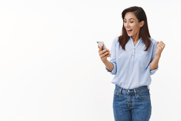 Cheerful triumphing adult 30s woman fist pump while reading excellent news, smiling broadly hold...
