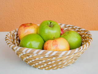 Red and green apples in the basket, at the white table
