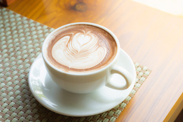 Coffee latte Art in white ceramic cup on wooden table in morning time