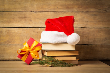 Obraz na płótnie Canvas Pile of books, Santa Claus hat, Christmas-tree decorations and Gifts on a wooden background. Holiday concept, christmas, christmas eve