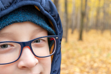 A teenage boy in late autumn park wearing trendy stylish eyeglasses close up outdoor, copy space