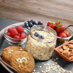 Tray with ripe organic bilberry raspberry strawberry oat cookies and almonds set on slate closeup