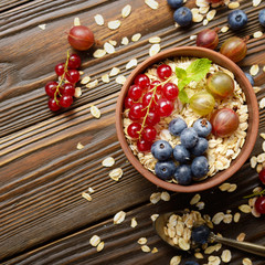 Flat lay view at oats in clay bowl with berries on wooden table