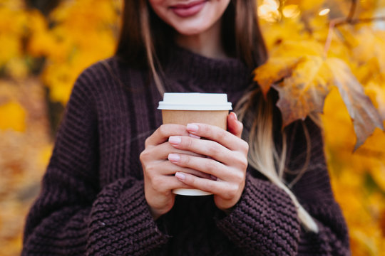 paper coffee cup in women's hands on autumn background