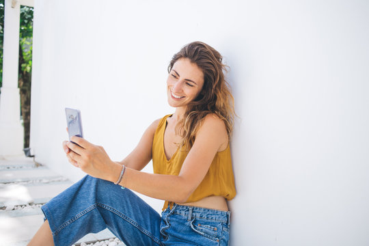 Content beautiful modern woman in casual wear sitting on floor taking selfie picture by mobile