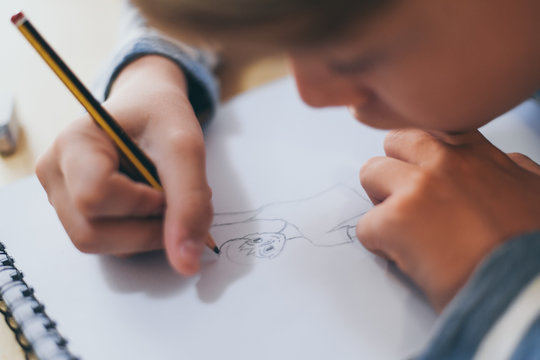 Close up view of student drawing with pencil. Boy doing homework writing on a paper. Kid hold a pencil and draw a manga at home. Teen drawing sitting at the table. Education art talent ability concept