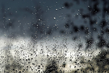 Rain drops on the window after rain. In the background are blurred outlines of trees and clouds.