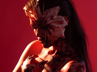 Blood Lily, scary and sexy Halloween look. Beautiful young brunette girl on red background.