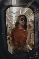 Fototapeta premium Beautiful girl in a red shirt and blue jeans in a subway train car.