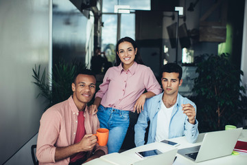 Fototapeta na wymiar Portrait of positive multicultural male and female employees posing near desktop with modern laptop device, group of architects collaborating during working processes enjoying friendly atmosphere
