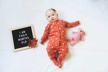 Four months old baby girl laying down on white background with letter board and teddy bear. Flat...