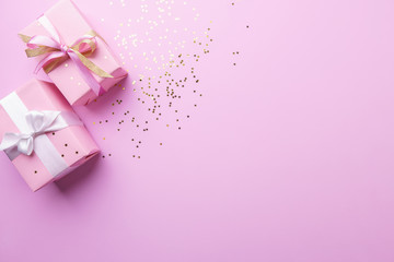Holiday design template with festive gift boxes wrapped with ribbons. Pink background studded with gold sparkling star shaped glitter confetti. Birthday, valentines, christmas celebration concept