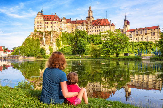 Family sit near medieval Sigmaringen Castle, Germany. Young woman and her child are by river in summer. 