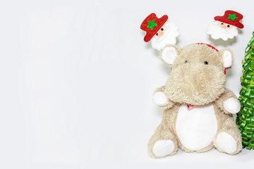 Cute teddy hippo, soft toy with christmas decoration on a head and a christmas tree on white background with copy space
