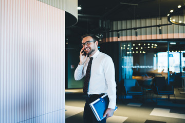 Smiling Caucasian male broker formally dressed feeling good from received news during phone call to business partner, happy man in optical eyewear communicate for consultancy about successful startup