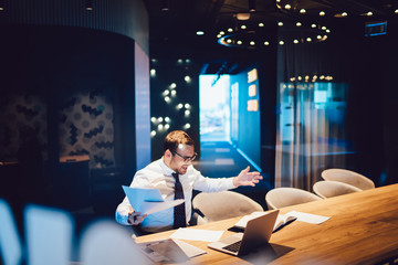 Emotional stressed businessman in nervous mood after overwork with laptop and paper documents, angry male office worker searching productive strategy for startup project unhappy with fail