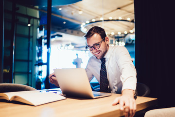Happy businessman sitting at office desk looking at computer screen browsing website and smiling...