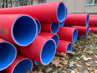 Many stacked red and blue pvc plastic plumbing tubes pipes lying on the ground outdoors