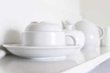 White ceramic coffee cups and saucers standing in a row on a shelf in kitchen