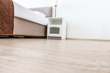 Empty white bedroom interior with copy space on the floor, low angle shot of a bed and a nightstand