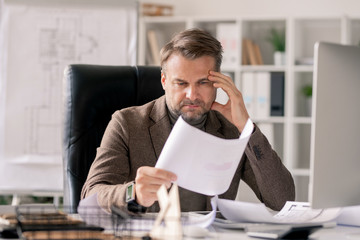 Pensive architect looking at sketch on paper while concentrating on work