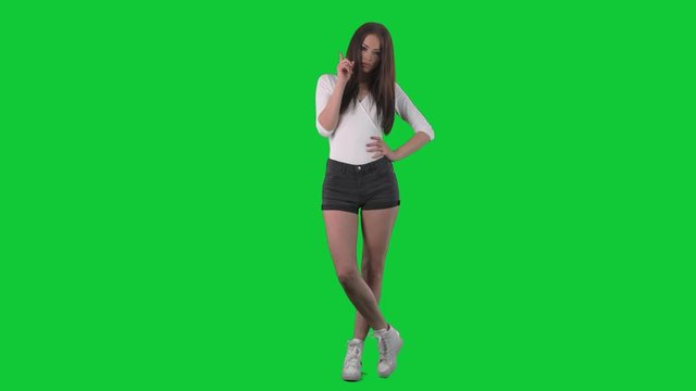 Strict serious displeased young pretty woman shaking finger with threats and warning. Full body over green screen background. 