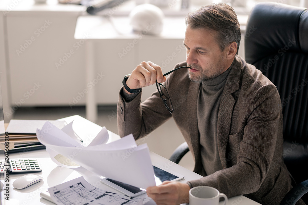 Poster Serious director of company or engineer looking through papers with sketches