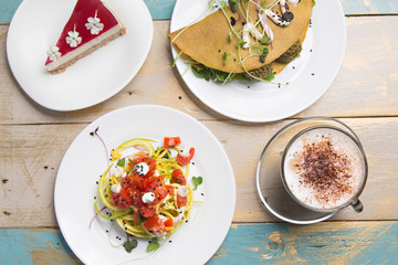 Healthy lunch, zucchini pasta, vegetable crepe and cappuccino coffee, on wooden table, top view.