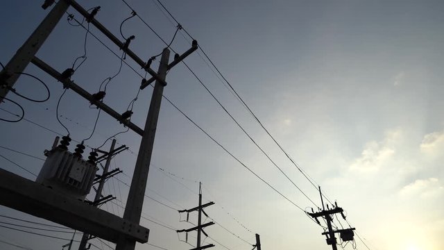 moving forward and looking up along high voltage transformer electrical line silhouette with bright blue sky and cloudy weather in evening time stock footage
