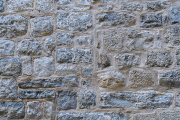 A fragment of an old stone wall made of rough stones. Background. Gray.