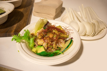 Green vegetarian salad with avocado, saffron, cucumber and chickpeas in a disposable plate on a wooden table