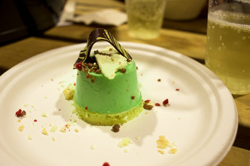 An avocado cheesecake dessert with dried berries and black chocolate on a disposable plate on a wooden table