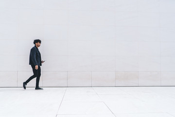 Casual African American man using tablet while walking along urban street