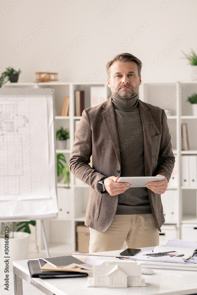 Poster Confident mature architect in formalwear using tablet while standing by desk