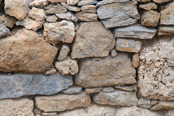 A fragment of an old stone wall made of rough stones. Background. Ocher. Gray.