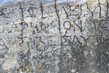 Half-erased ancient Greek letters embossed on an old gray marble slab covered with cracks and mold.